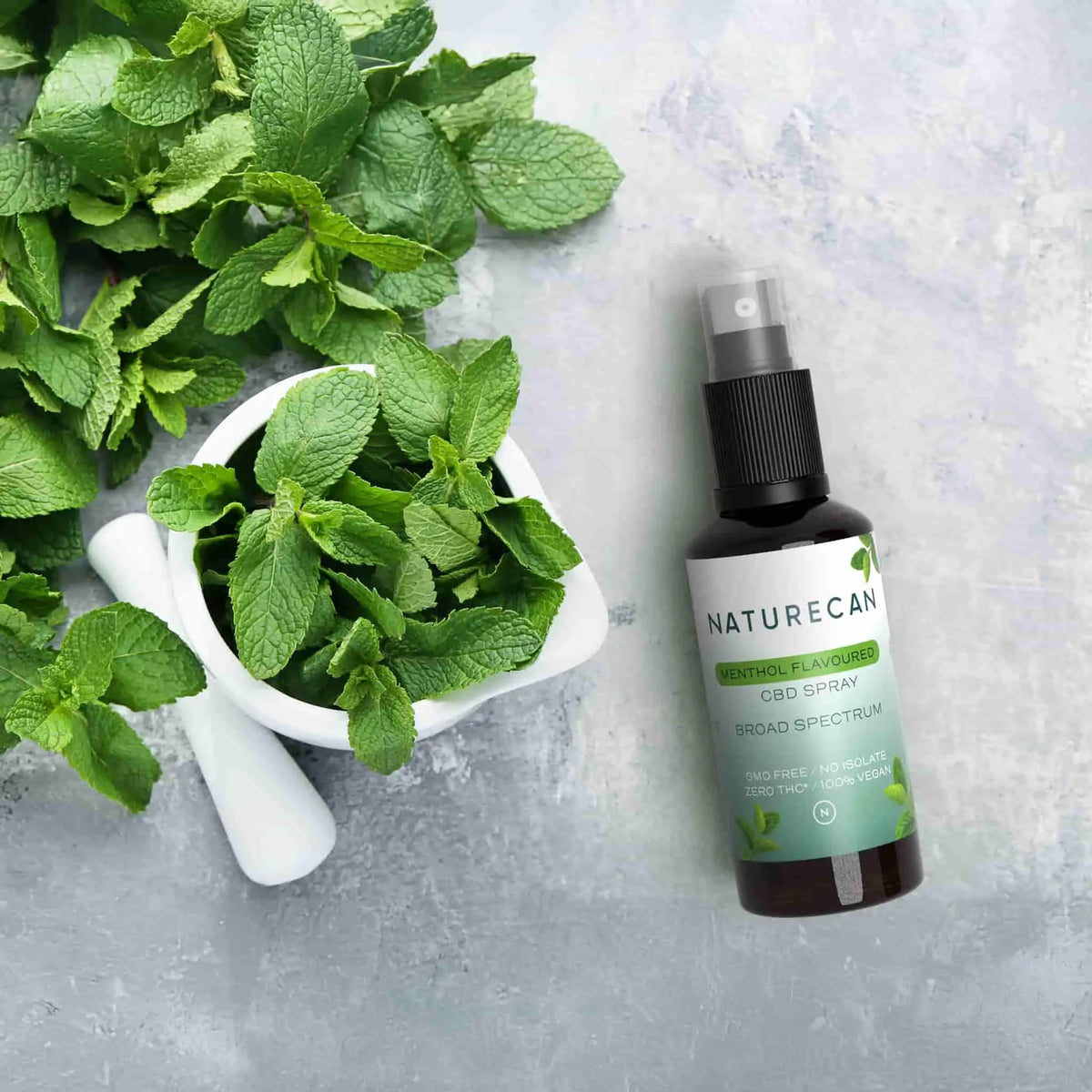 Naturecan Menthol CBD Spray lifestyle – brown spray bottle beside fresh mint leaves in a marble mortar and pestle on stone surface